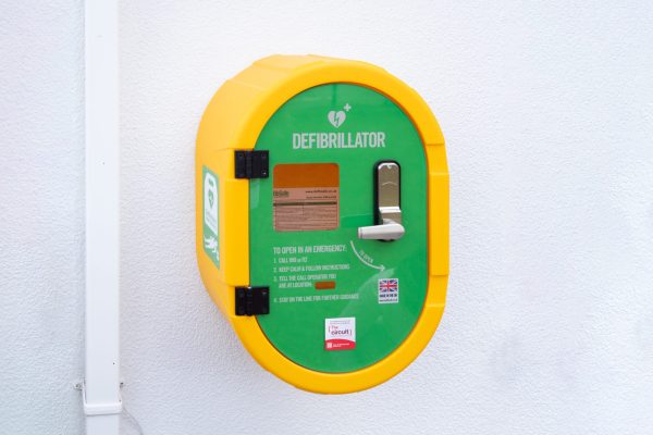 A photo of a yellow and green defibrillator device mounted on an external wall.