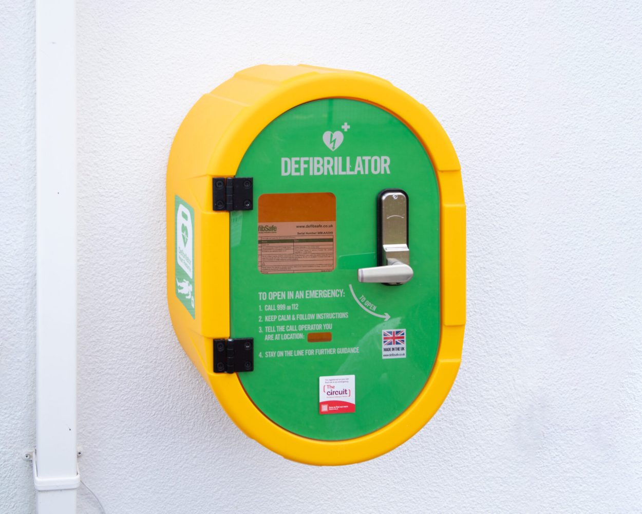 A photo of a yellow and green defibrillator device mounted on an external wall.