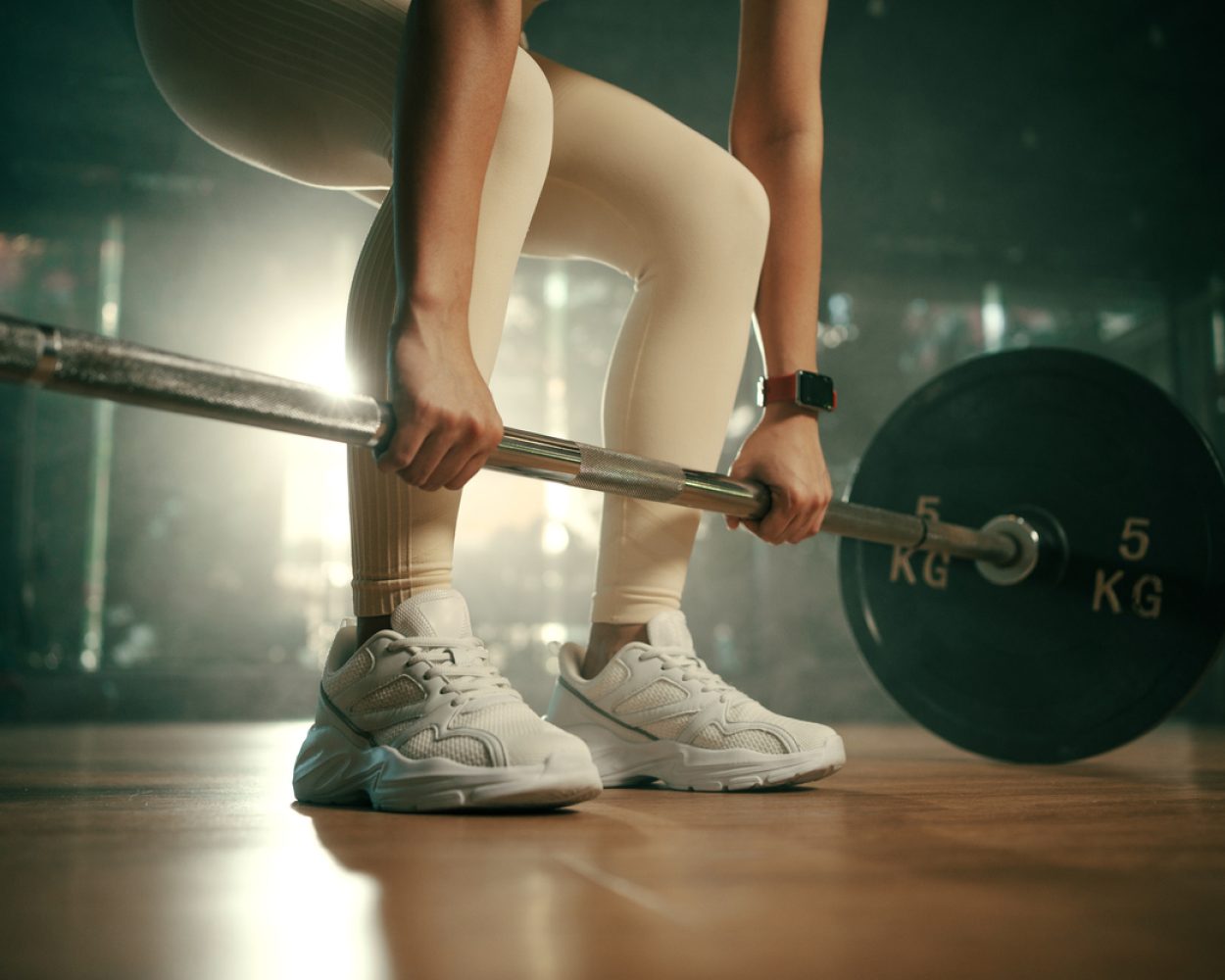 Young woman doing deadlift with heavy bar in gym, strong female athlete with muscular body lifting weights, exercising with barbell.