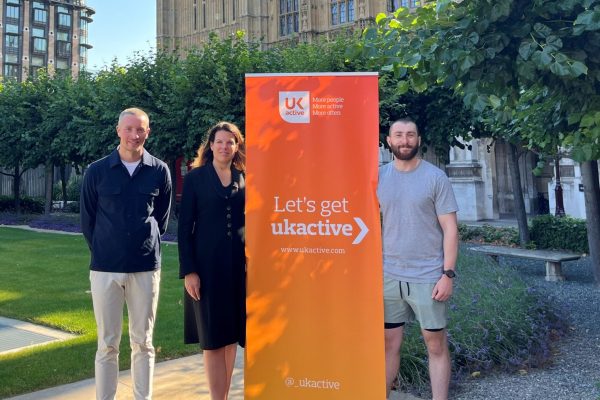 Ben Sandham, Caroline Nokes and Stephen McLoughlin standing in front of Westminster with an orange ukactive-branded banner