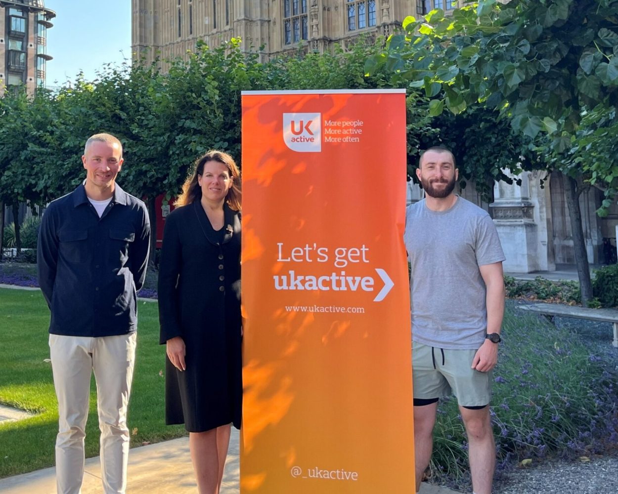 Ben Sandham, Caroline Nokes and Stephen McLoughlin standing in front of Westminster with an orange ukactive-branded banner