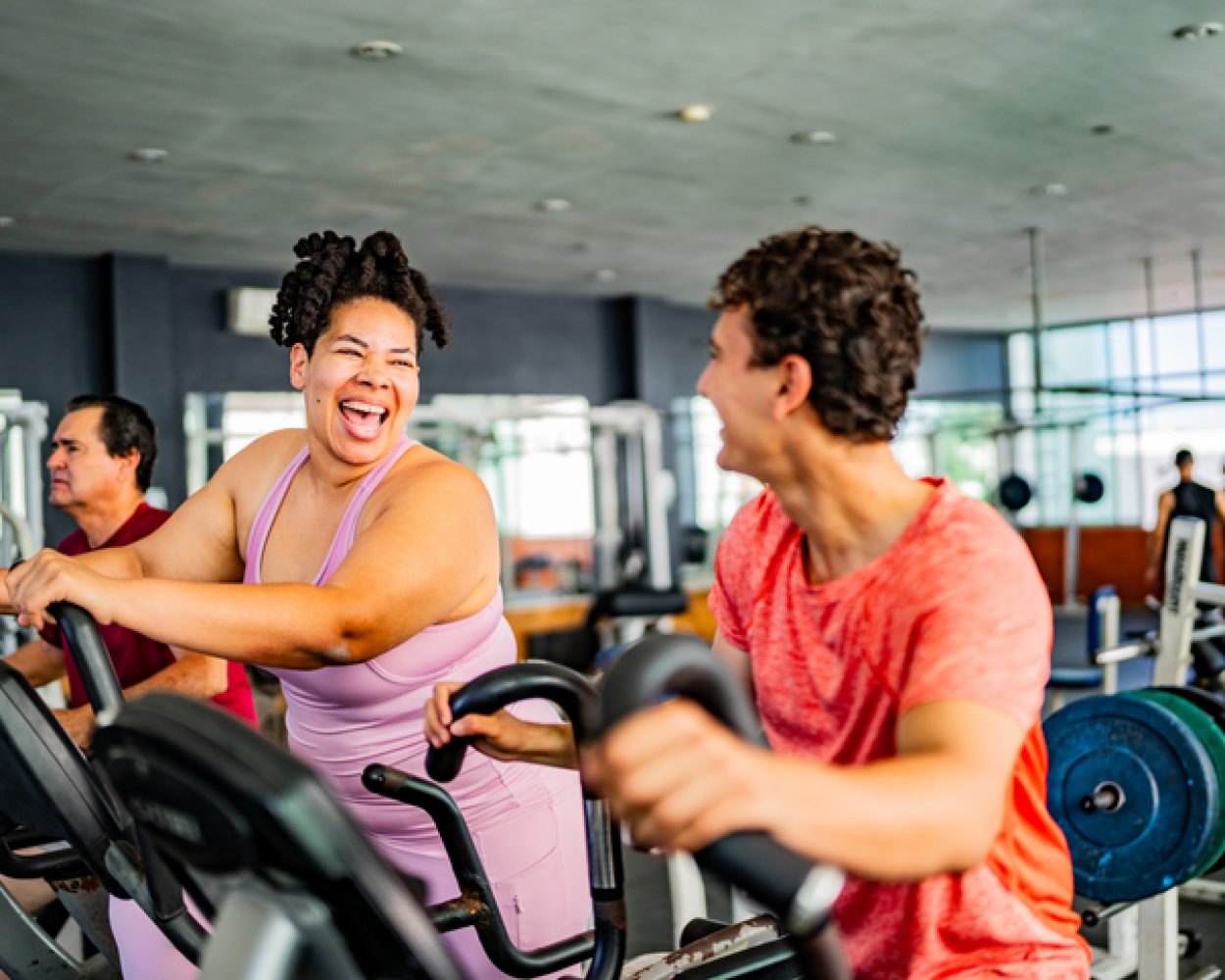 Friends talking while exercising on elliptical cross trainer at gym
