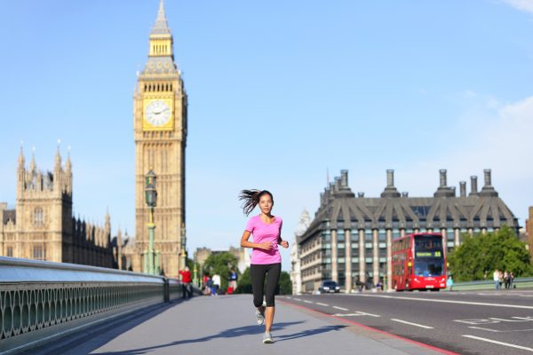 London lifestyle woman running near Big Ben. Female runner jogging training in city with red double decker bus. Fitness girl smiling happy on Westminster Bridge, London, England, United Kingdom.