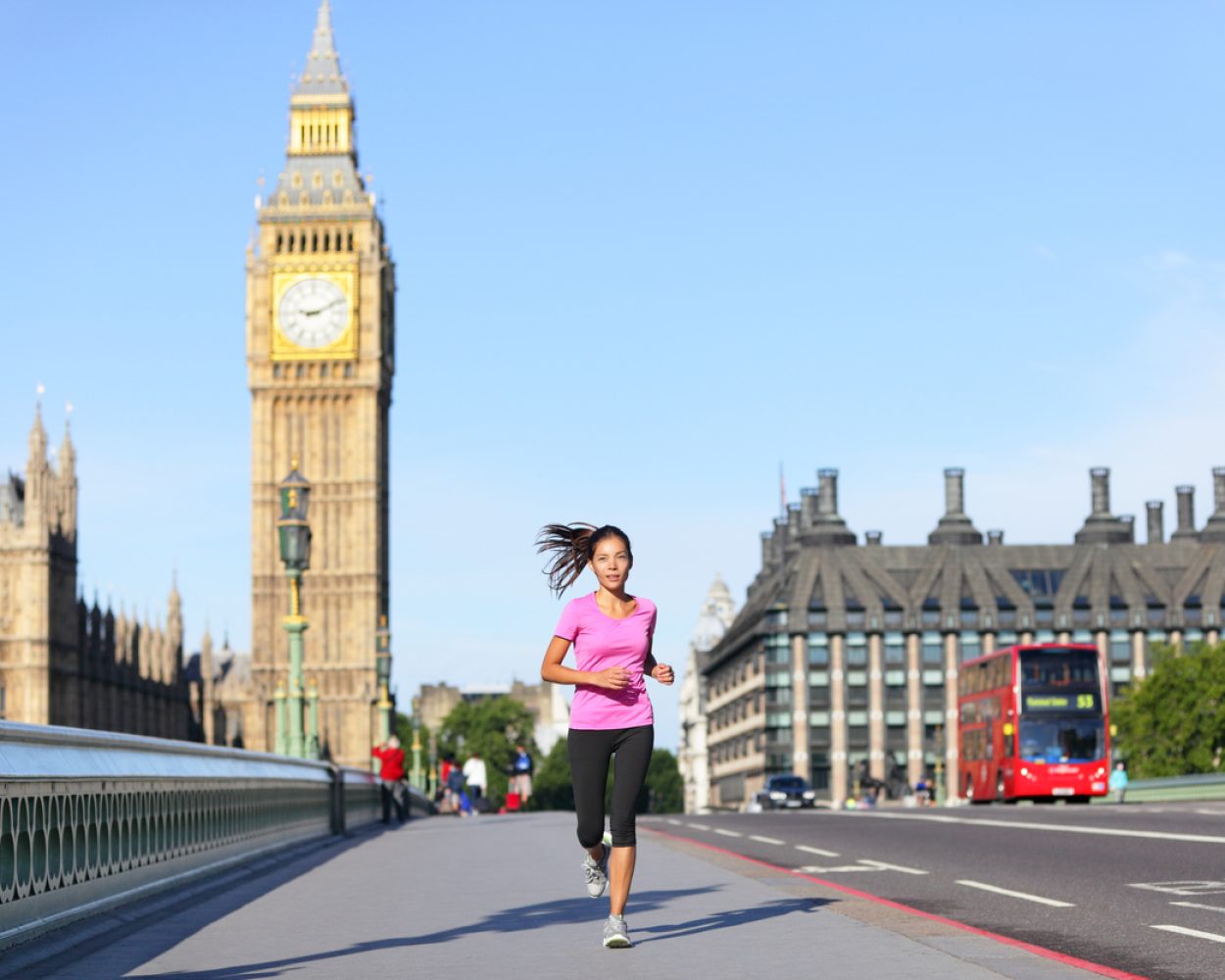London lifestyle woman running near Big Ben. Female runner jogging training in city with red double decker bus. Fitness girl smiling happy on Westminster Bridge, London, England, United Kingdom.