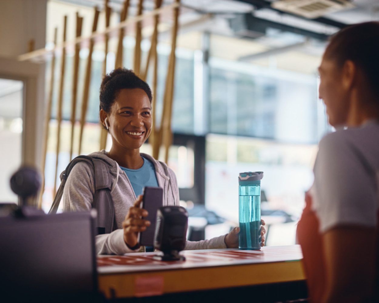 Happy black sportswoman using smart phone while checking in at the gym.