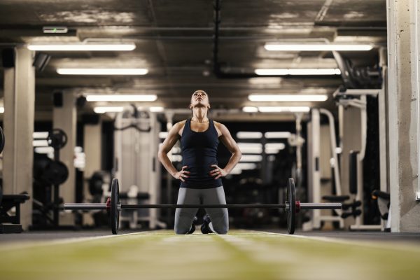 A female bodybuilder is motivating herself and preparing to lift barbell while kneeling in a gym.