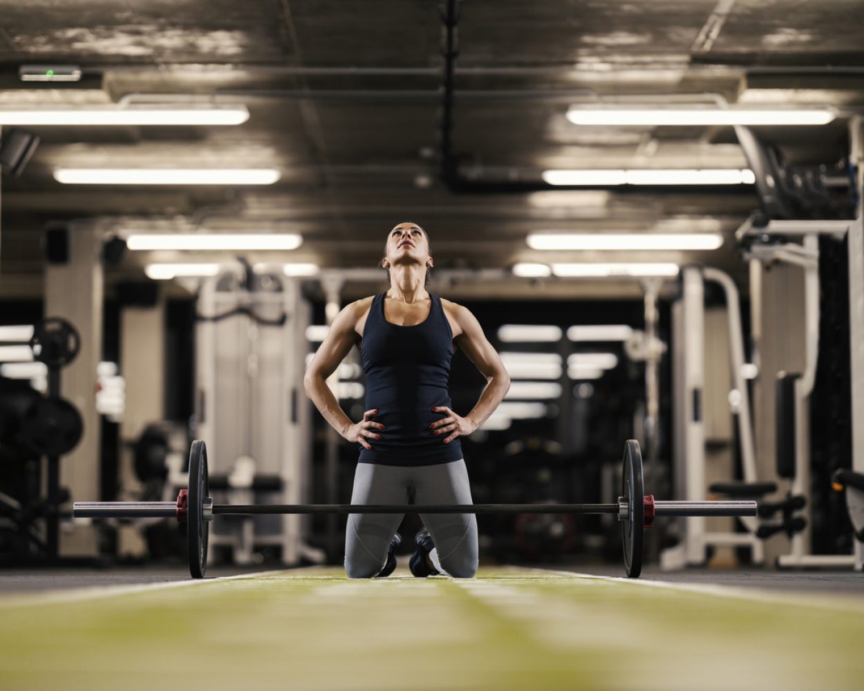 A female bodybuilder is motivating herself and preparing to lift barbell while kneeling in a gym.
