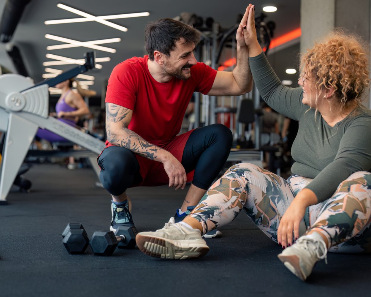 Happy male coach giving young woman high-five after successful sports training session in gym