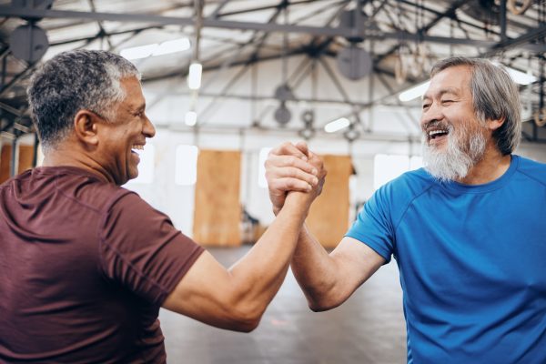 Two older males shaking hands within a fitness facility.