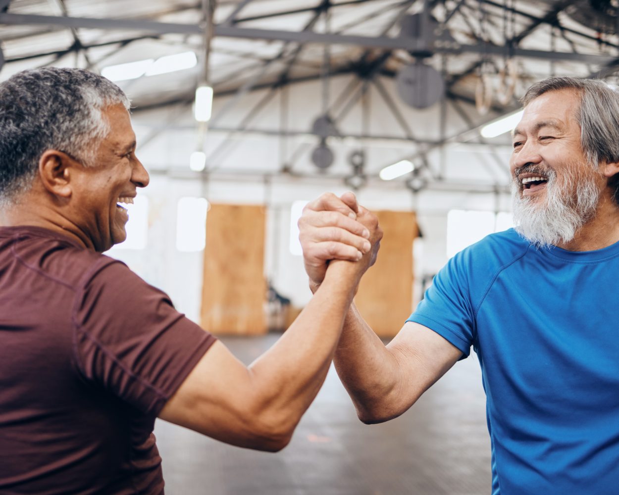 Two older males shaking hands within a fitness facility.