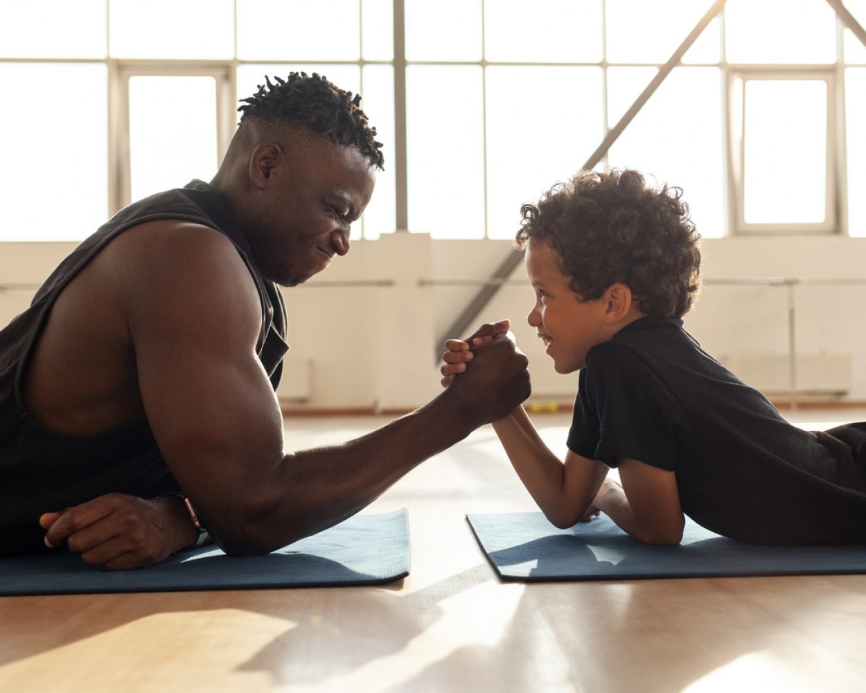 african american boy 9 years old competes with dad in arm wrestling, father trains his son and tests his strength