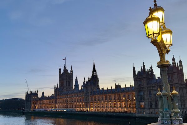 The Houses of Parliament in Westminster, London at dusk with an historic lamp on Westminster Bridge in the foreground.