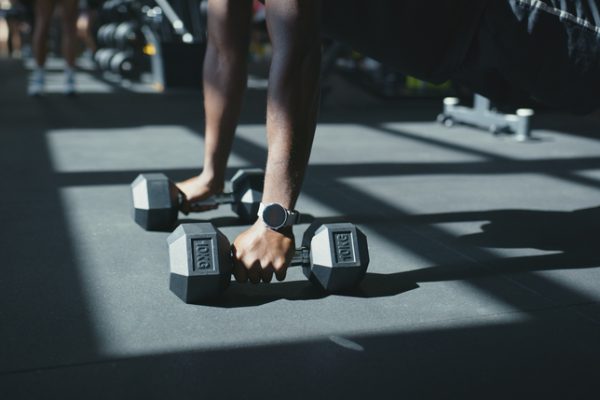 Hands, dumbbells and push up on floor at gym for upper body strength, training and routine for fitness. Person, bodybuilder and equipment with workout, challenge or exercise for muscle growth at club
